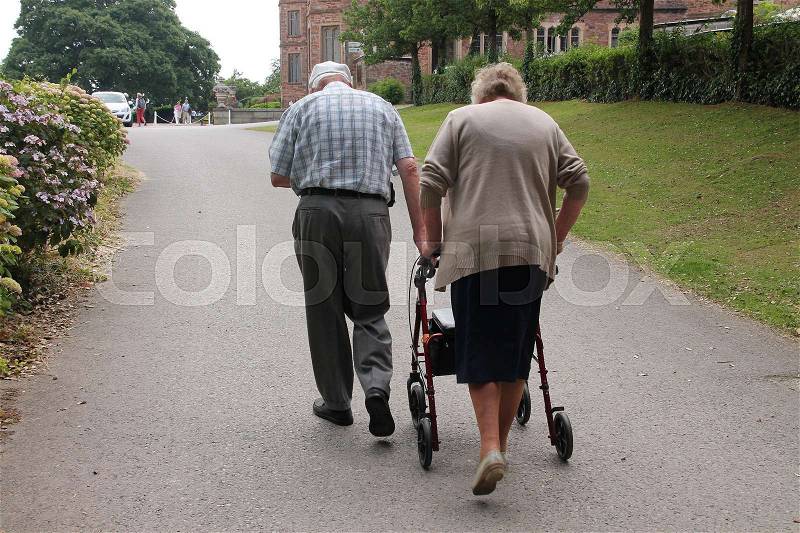 The old man helps his wife with the walker to the top in the park in England in the summer, stock photo