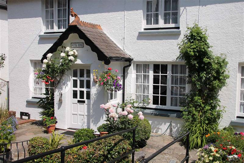 Striking white cottage, hanging baskets with blooming plants and a wonderful garden in the village in the summer in England, stock photo