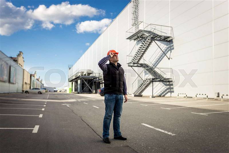 Full length portrait of male worker posing on parking of industrial building, stock photo