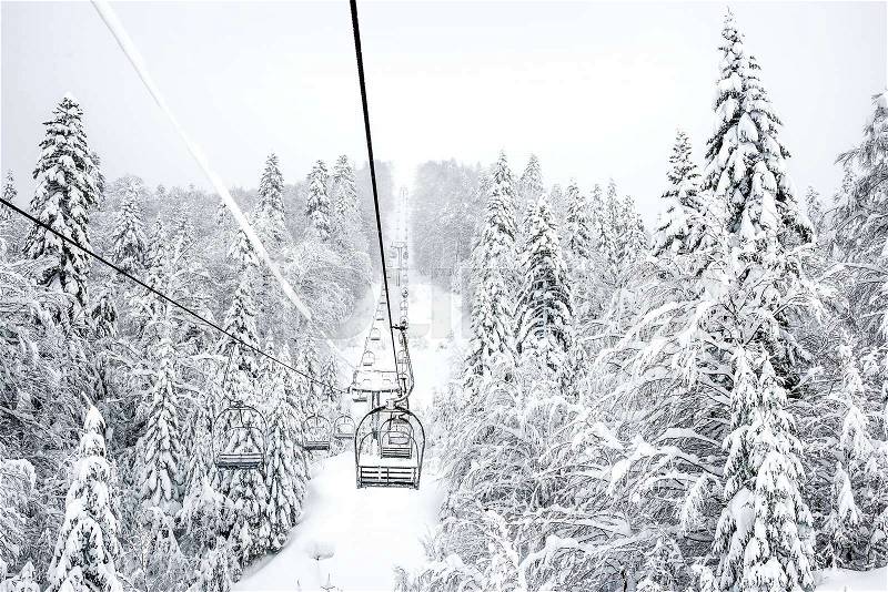Old cable ski lift with no passangers going across the coniferous forest in \'Kolasin 1450\' mountain ski resort near the town of Kolasin in Montenegro after a heavy snowfall on a winter day, stock photo