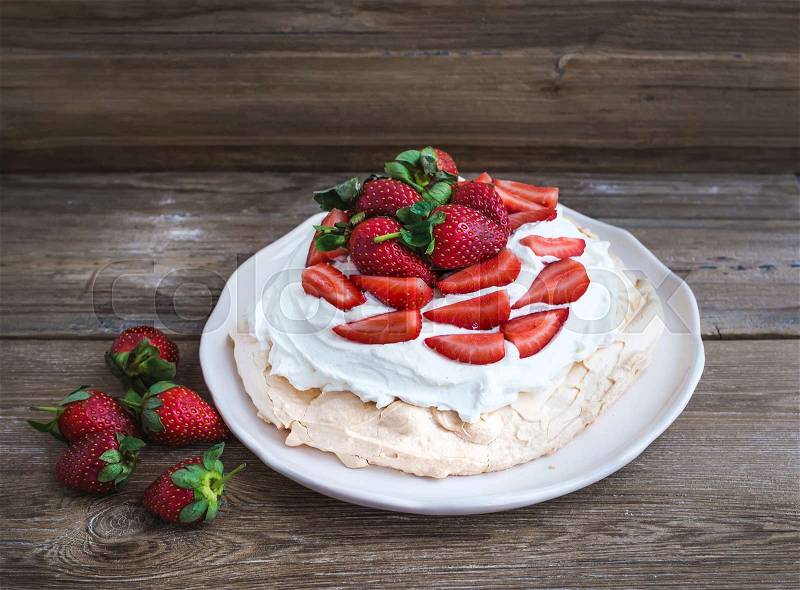 Rustic Pavlova cake with fresh strawberries and whipped cream over a rough wood background, stock photo
