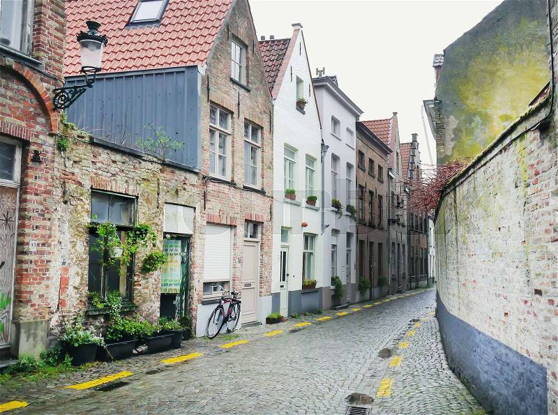 An old medieval empty side street of Bruges, Belgium, with a bike parked at one side, stock photo