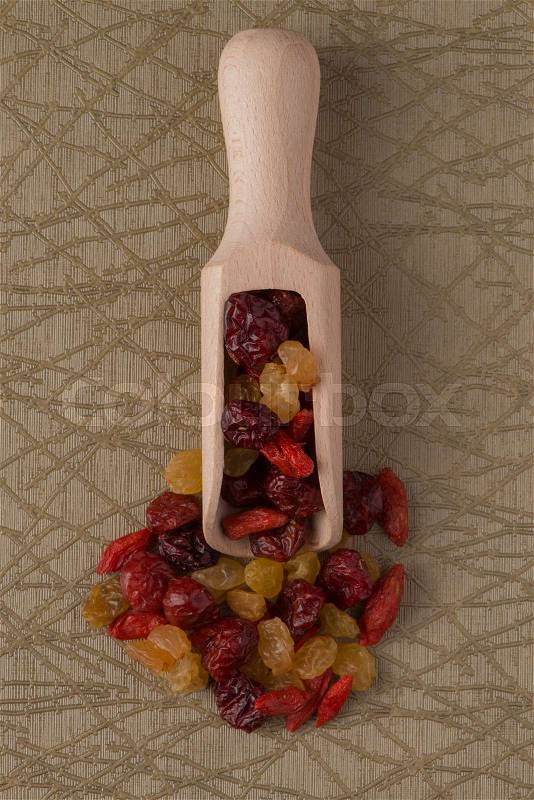 Top view of wooden scoop with mixed dried fruits against green vinyl background, stock photo