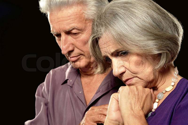 Sad elderly couple on a black background, stock photo
