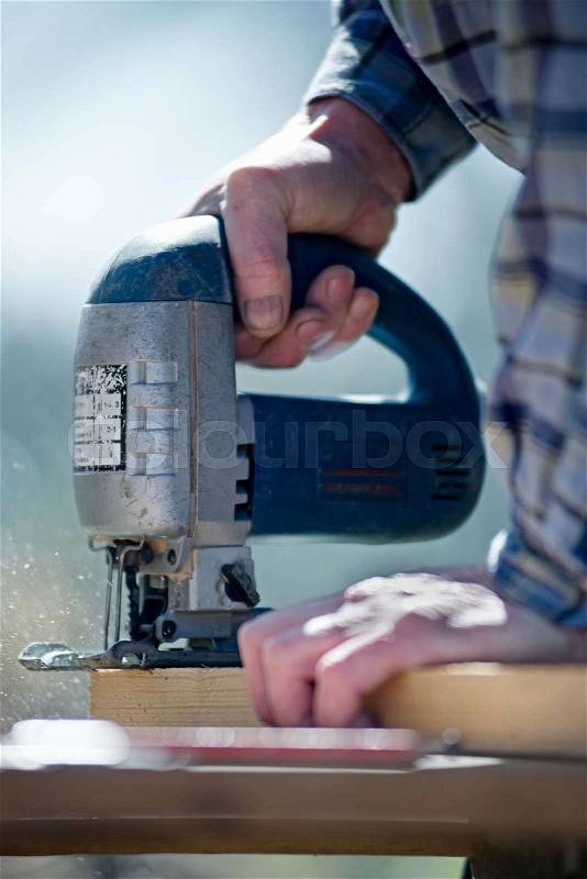 Hands of man carpenter builder working with electric jigsaw and wood with a blurred background, stock photo