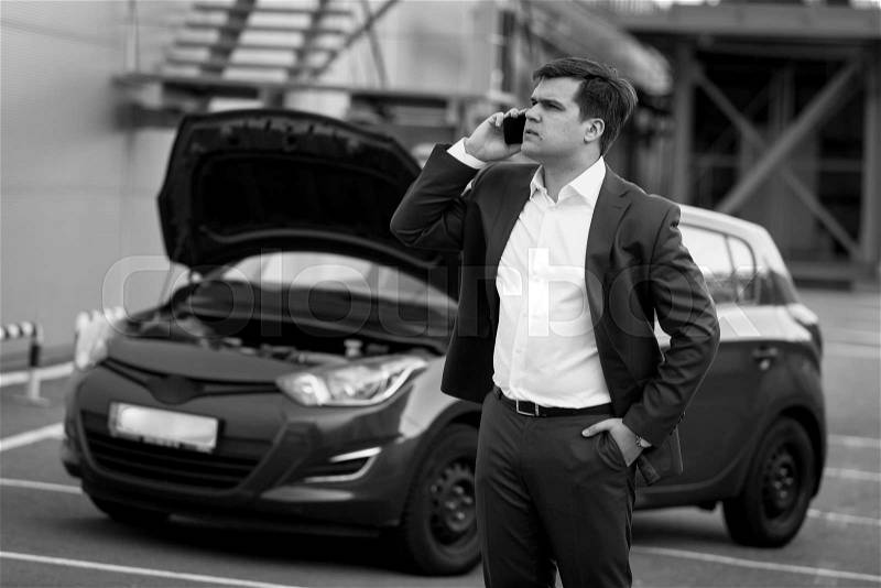 Black and white portrait of man calling in technical service to evacuate broken car, stock photo
