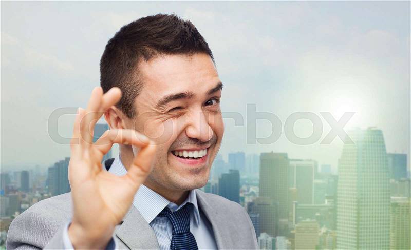 Business, people, gesture and success concept - happy smiling businessman in suit showing ok hand sign over city background, stock photo