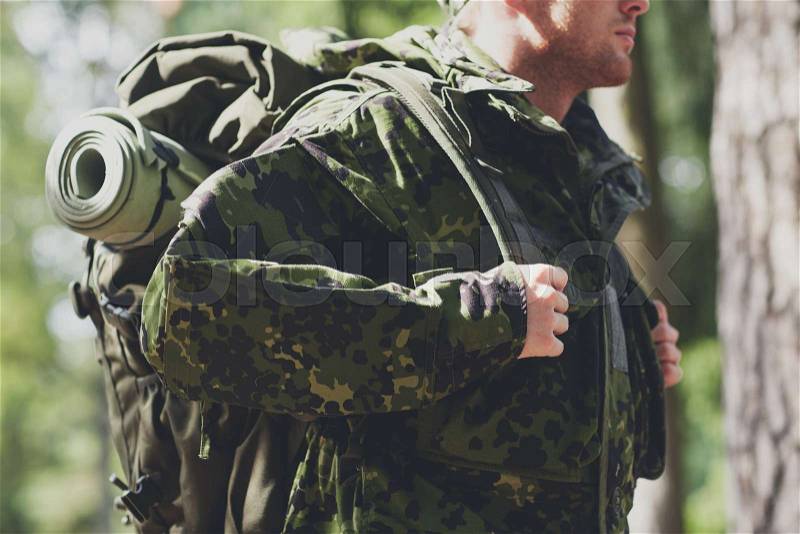 War, hiking, army and people concept - close up of young soldier, ranger or hunter with backpack walking in forest, stock photo
