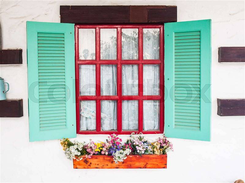 Opened wooden shutter light green window on white wall with flower bed, stock photo