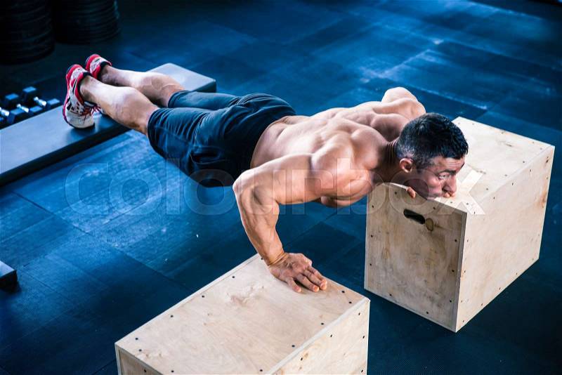 Muscular man doing push ups on fit box and bench at gym, stock photo