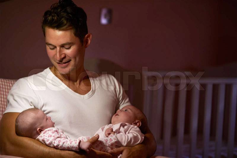 Father At Home Cuddling Twin Baby Daughters In Nursery, stock photo