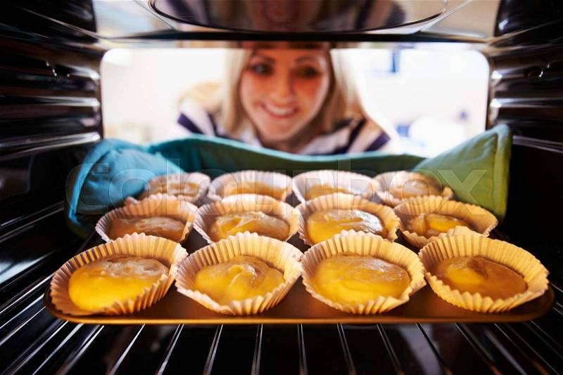 Woman Putting Cupcakes Into Oven To Bake, stock photo