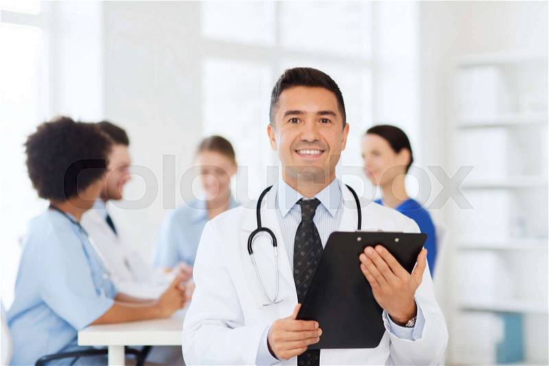 Clinic, profession, people and medicine concept - happy male doctor with clipboard over group of medics meeting at hospital, stock photo