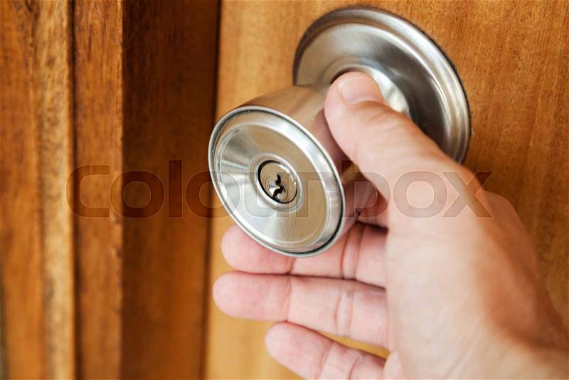Male hand opening shining metal door handle in closed wooden door, photo with selective focus and shallow DOF, stock photo