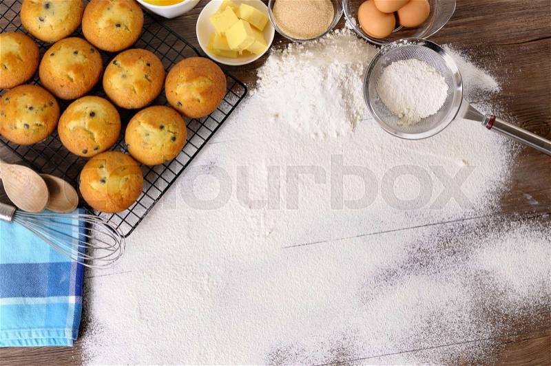 Baking background with dusted flour on a dark wood table with freshly baked muffins and ingredients, stock photo