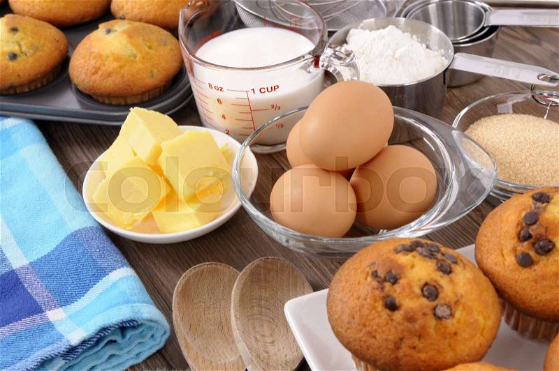 Baking ingredients on a wood table with freshly baked muffins, stock photo