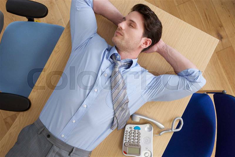 Overhead View Of Businessman Lying On Desk In Office, stock photo