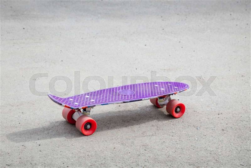 Small size modern purple plastic skateboard stands on an empty urban asphalt road, stock photo