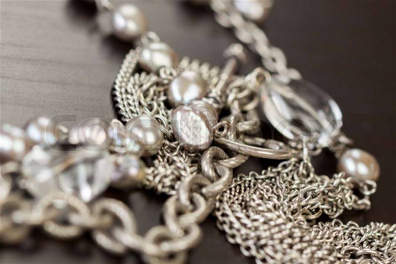 Assorted silver costume jewellery with a jumbled pile of chains with different shaped links, a clear crystal bead and a necklace of round silver beads with focus to the chains, stock photo