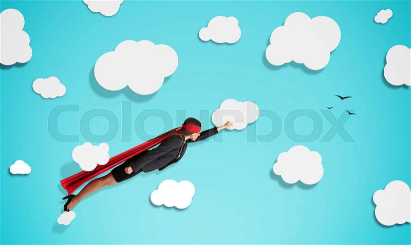 Superwoman in red mask and cloak flying through paper clouds over blue background, stock photo