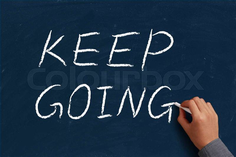Keep Going on blue chalkboard with the hand of businessman, stock photo