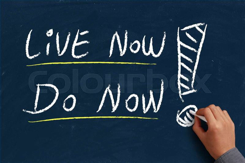 Live now do now on blue chalkboard with the hand of businessman, stock photo