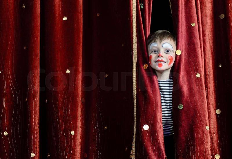 Young Boy Wearing Clown Make Up Peering Out Through Opening in Red Stage Curtains, stock photo