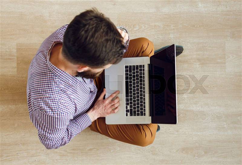 Top view of young man sitting on the floor and working with a laptop, stock photo
