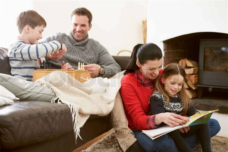 Family Relaxing Indoors Playing Chess And Reading Book, stock photo