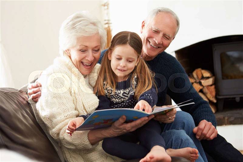 Grandparents And Granddaughter Reading Book At Home Together, stock photo