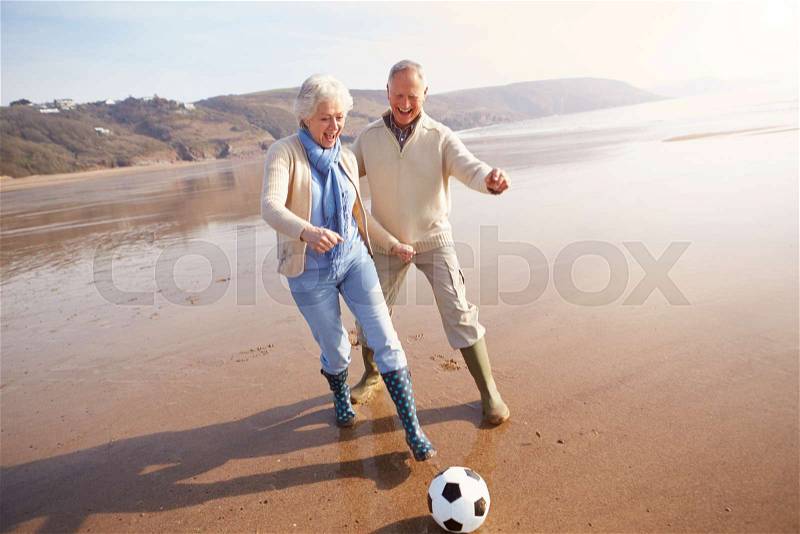 Senior Couple Playing Football On Winter Beach, stock photo