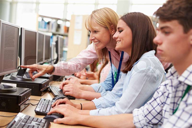 Students Working At Computers In Library With Teacher, stock photo