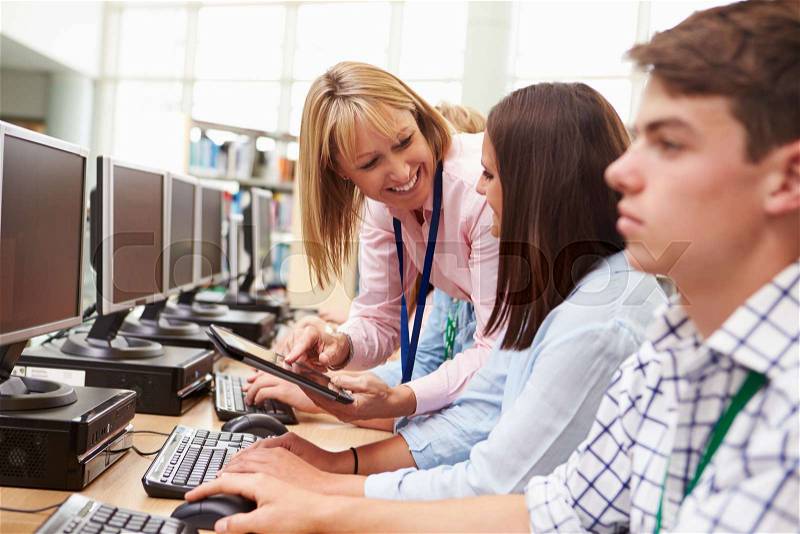 Students Working At Computers In Library With Teacher, stock photo