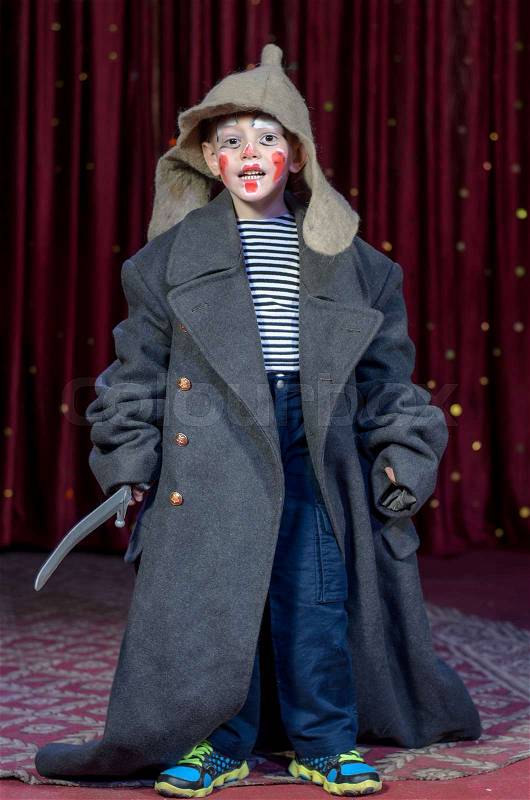 Young Boy Dressed in Over Sized Grey Coat and Floppy Hat Holding Prop Toy Sword with Face Painted in Clown Make Up, Standing on Stage Looking at Camera, stock photo