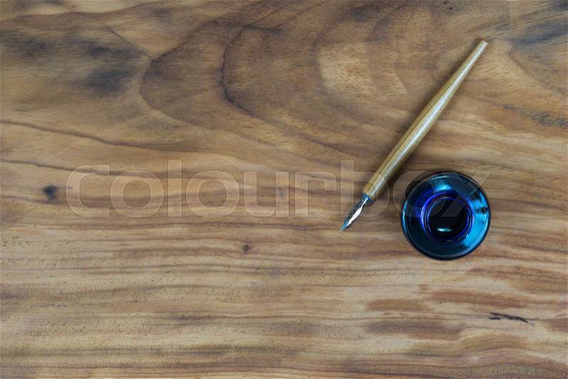 Old fashioned ink dip pen for writing or drawing on wooden table with parchment paper background, stock photo