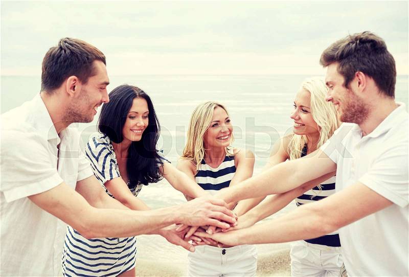 Friendship, happiness, unity and people concept - smiling friends putting hands on top of each other, stock photo