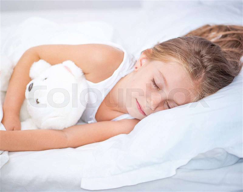 Six year old girl sleeping in white bed with her teddy bear, stock photo