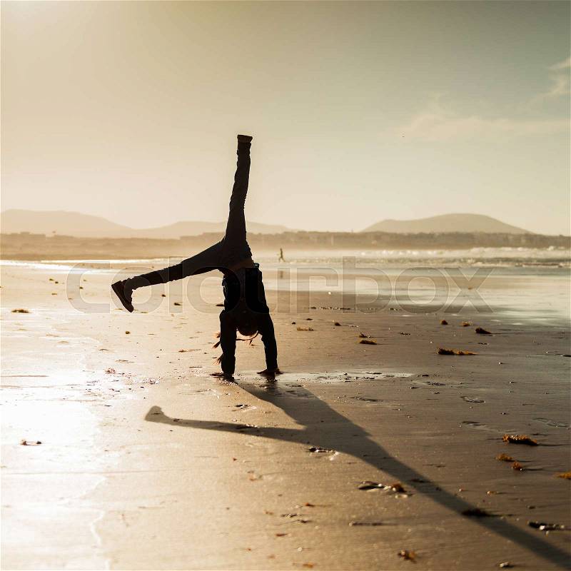 Little gymnast silhouette on the beach at sunset, stock photo