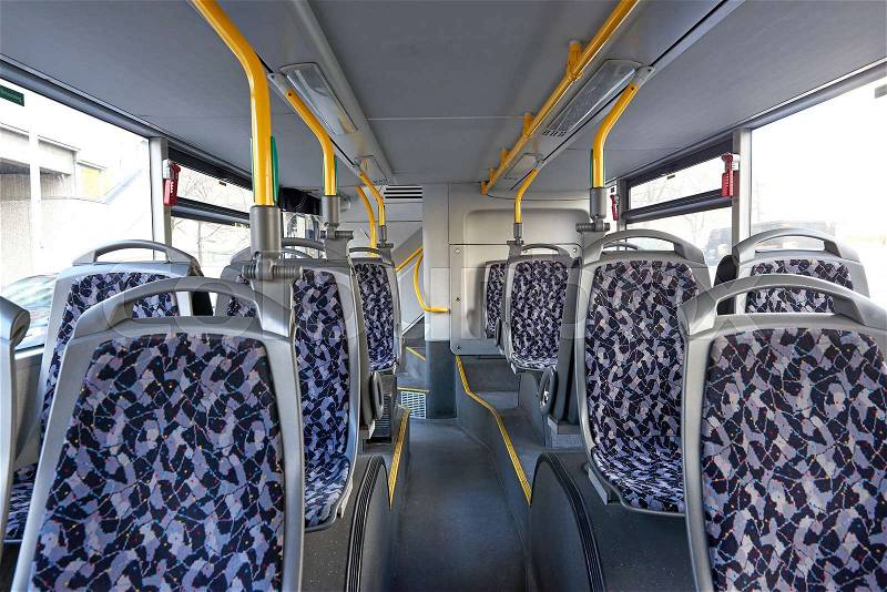 Empty bus seats with a blue pattern and yellow handlebars above them, stock photo