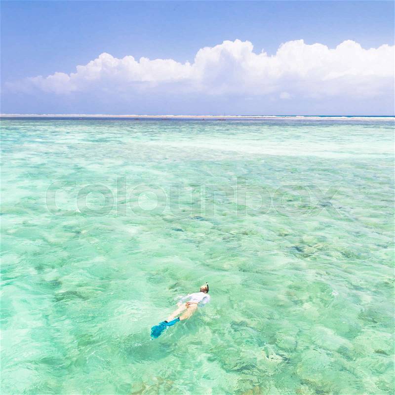 Young woman snorkeling in clear shallow sea of tropical lagoon with turquoise blue water and coral reef, near exotic island. Mnemba island, Zanzibar, Tanzania, stock photo