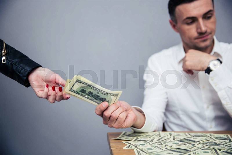 Unhappy man giving money to woman over gray background, stock photo