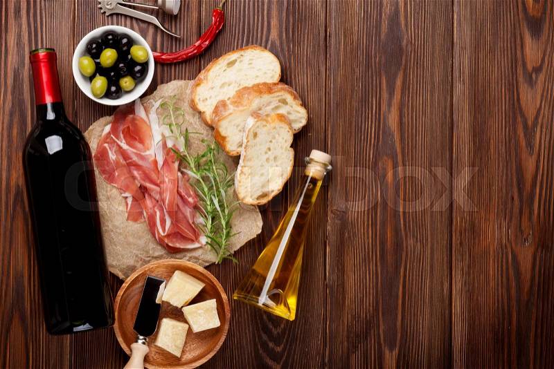 Prosciutto, wine, olives, parmesan and olive oil on wooden table. Top view with copy space, stock photo
