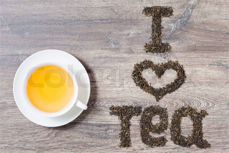 Words I love tea made of green tea leaves on wood background. Text on the right. A cup of tea on the left, stock photo