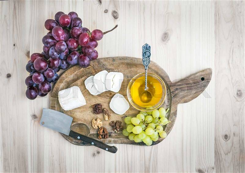 Goat brie cheese with fresh grapes and honey on a rustic wooden board over a light wood background. Top view, stock photo