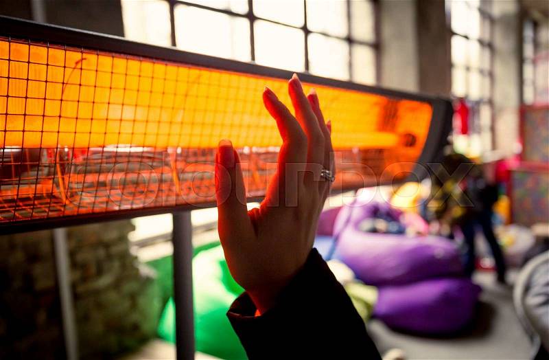 Closeup shot of woman warming hands at infrared heater, stock photo