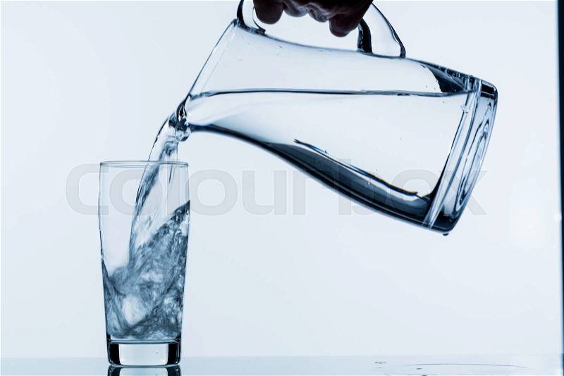Pure water is emptied into a glass of water from a jug. fresh drinking water, stock photo