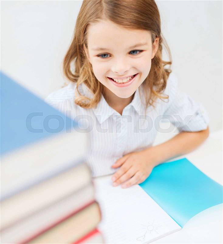 Education and school concept - smiling little student girl with many books at school, stock photo