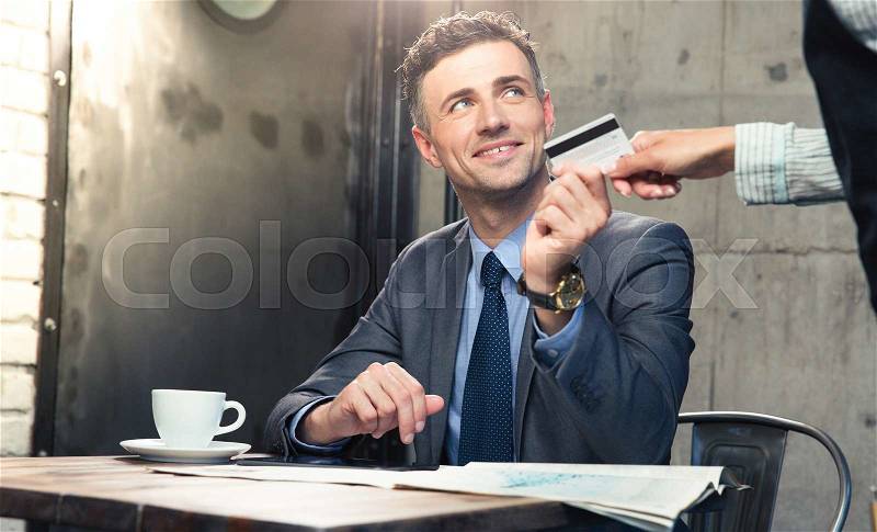 Handsome man giving bank card to waiter in cafe, stock photo