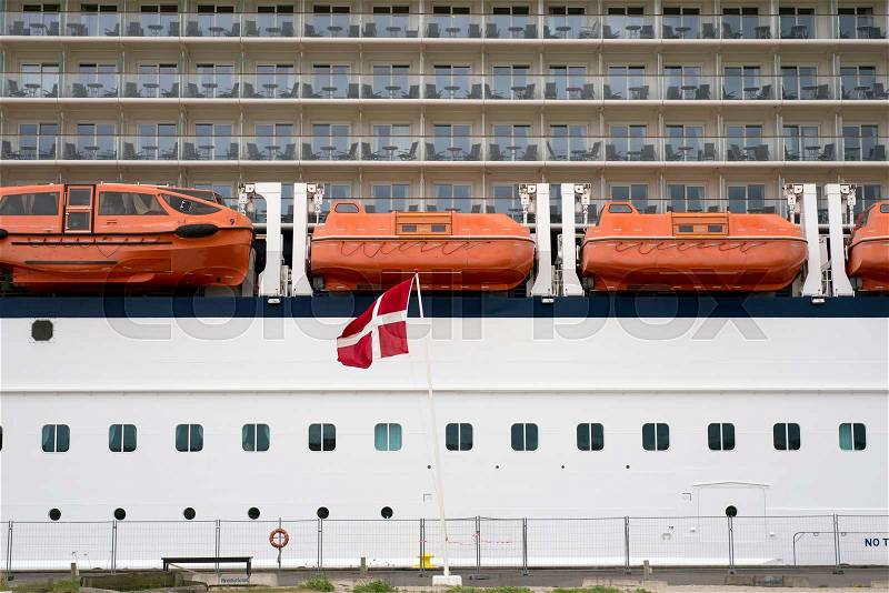 Side view of cabins on cruise liner with lifeboats and Danish flag blowing in tge wind on Fredericia harbor. No people and ship are unrecognizable, stock photo