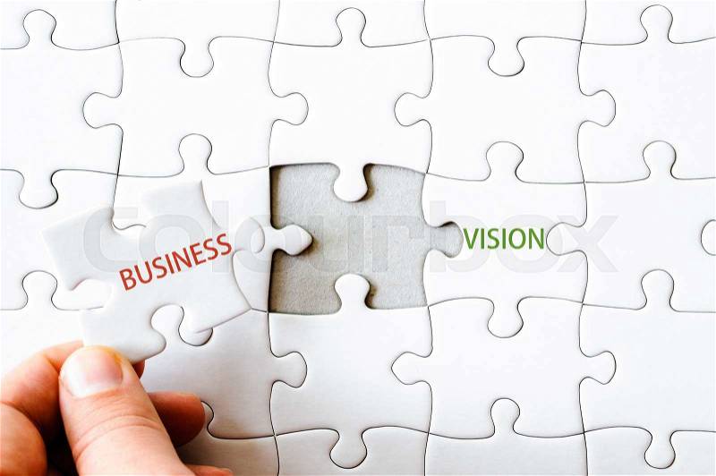 Hand with missing jigsaw puzzle piece completing the words BUSINESS VISION. Business concept image for completing the final puzzle piece, stock photo